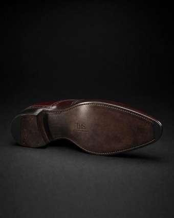 Close-up of a leather shoe sole with a dark antiqued edge and blind-embossed maker's mark